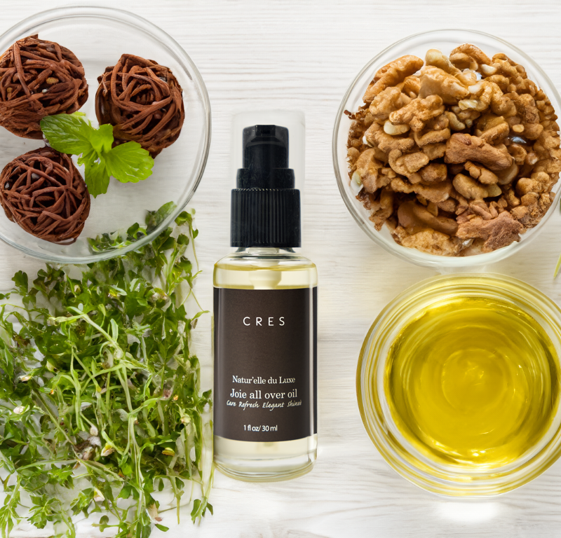 CRES Joie All Over Oil bottle with clean, minimalist packaging, surrounded by natural botanical ingredients like shea butter and jojoba.