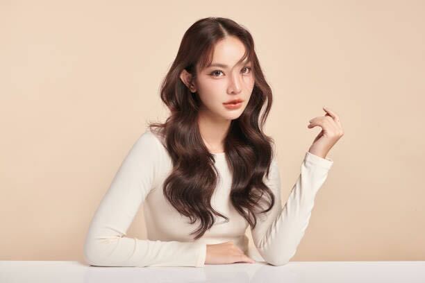 Thai actress Freen with long glossy curls, center-parted hairstyle, and bold eye makeup, showcasing 2025 Asian beauty trends.