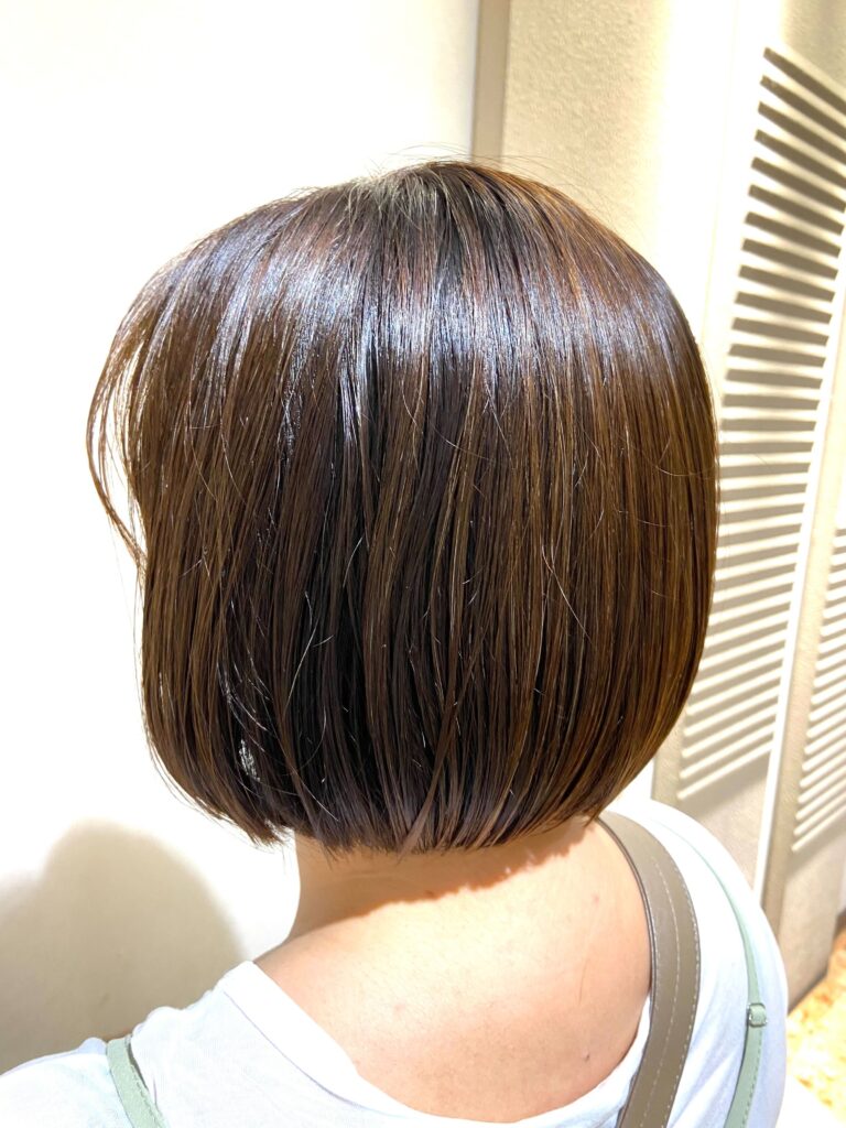 Woman with a sleek, jaw-length Teri Bob—blunt cut with no curves, tucked behind the ears for a polished summer look.