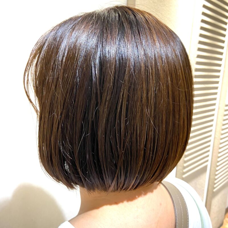 Woman with a sleek, jaw-length Teri Bob—blunt cut with no curves, tucked behind the ears for a polished summer look.